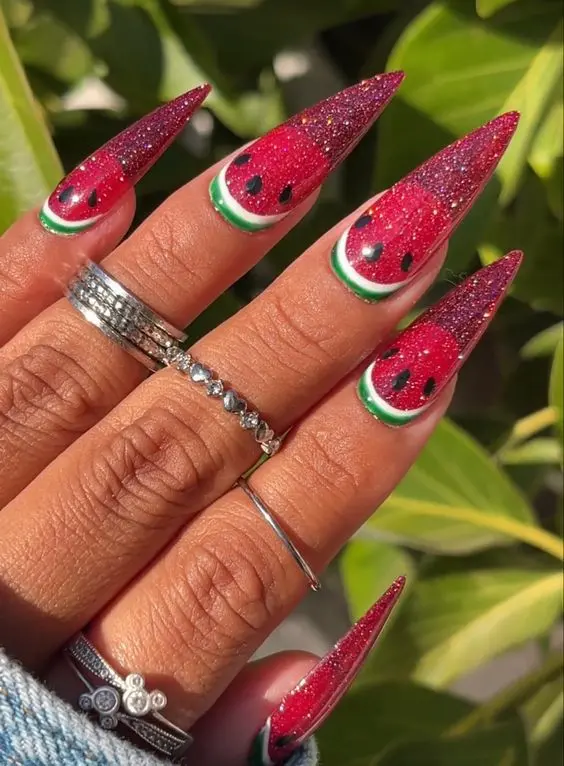 Glittery red stiletto nails featuring a watermelon design with green rind accents make for a sparkling, juicy summer statement.