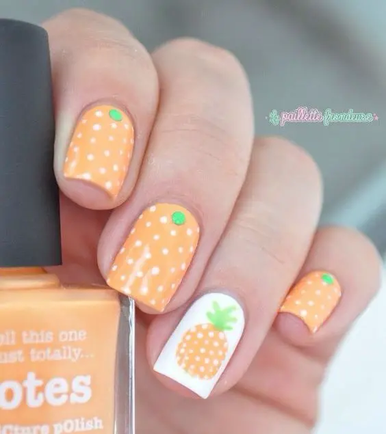 Short, square nails painted in a warm peach tone, featuring white polka dots and a charming pineapple design, perfectly encapsulate a tropical summer vibe.