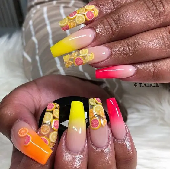 Vibrant summer-themed nails with ballerina form, showcasing a citrus blast of lemon and orange slices against a gradient yellow-pink background.