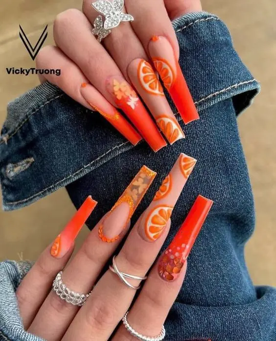 Vibrant summer nail design featuring long, fiery orange nails with citrus fruit accents, perfect for making a bold statement in the sunny season.