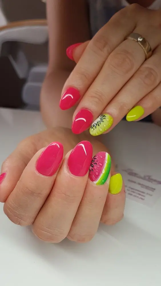 Lively summer manicure with bright pink and lime nails, featuring a watermelon design on the ring finger, adding a playful touch to the oval-shaped nails.