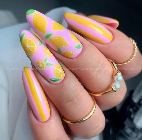 Sweet and tangy lemon patterns dance over pink and yellow striped nails, creating a summery confection of bright, playful charm for the warm season.