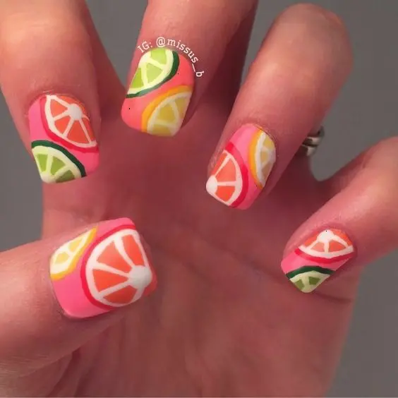 Short, square nails with a coral base showcase citrus segments in a refreshing pattern, perfect for a zesty summer look.