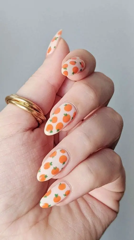 Almond-shaped nails in a pastel peach base sprinkled with adorable orange fruit patterns offer a fresh, sweet summer look that\'s deliciously on-trend.