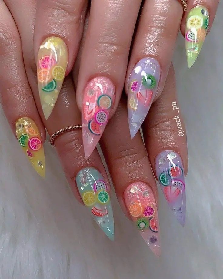 Long, stiletto nails boast a translucent base with a colorful array of fruit slices, creating a vibrant, summer nail art collage.