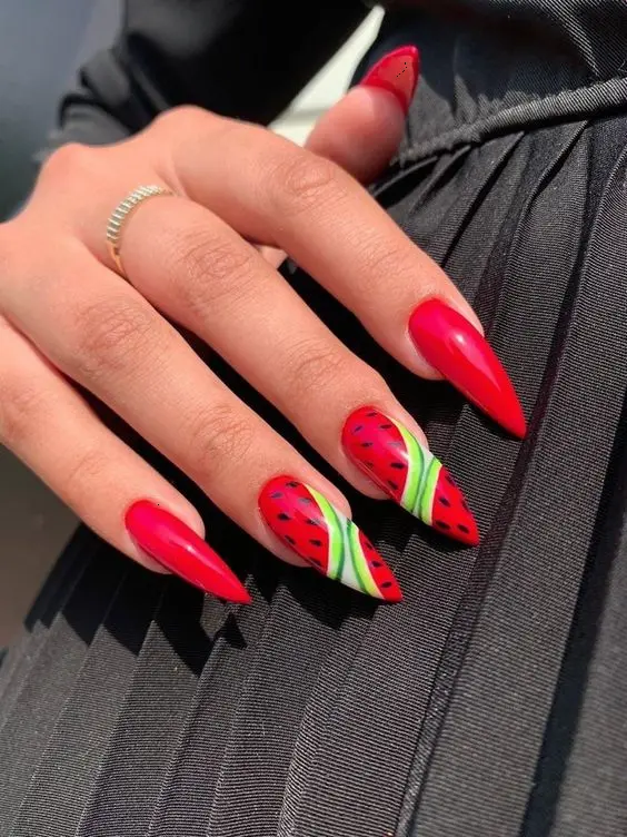 Stiletto nails in radiant red feature detailed watermelon slices on the tips, creating a striking contrast perfect for a bold summer look.