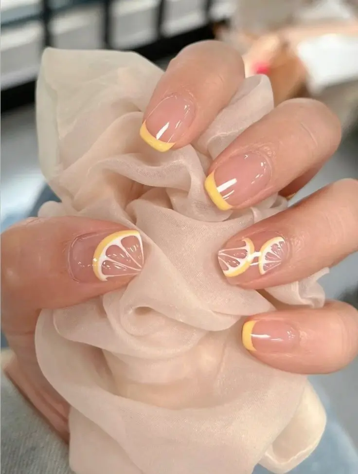 A delicate summer look with transparent nails, accented with bright yellow tips and whimsical lemon slice decals for a subtle yet charming vibe.