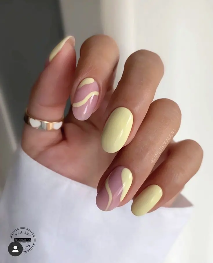 Rounded nails painted in pastel yellow with wavy designs on a nude base create a soft and trendy look. The subtle waves add a touch of modern elegance, perfect for a sophisticated summer style.