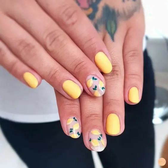 These nails feature a soft yellow polish on short, oval shapes with accent nails showcasing lemons and leaves on clear bases. The fresh, citrus-inspired design brings a bright and cheerful summer feel to this elegant look.