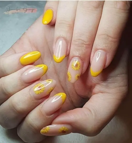 These nails feature a combination of yellow French tips and sunflower designs on clear bases. The almond-shaped nails are adorned with detailed floral accents, adding a touch of brightness and cheerfulness, ideal for summer.