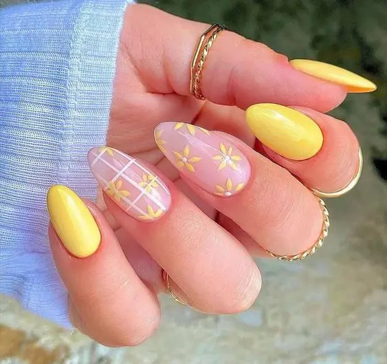 This nail design combines bright yellow nails with floral accents on a clear base. The almond-shaped nails feature yellow daisies and white grid patterns, creating a fresh and cheerful summer look perfect for any sunny day.