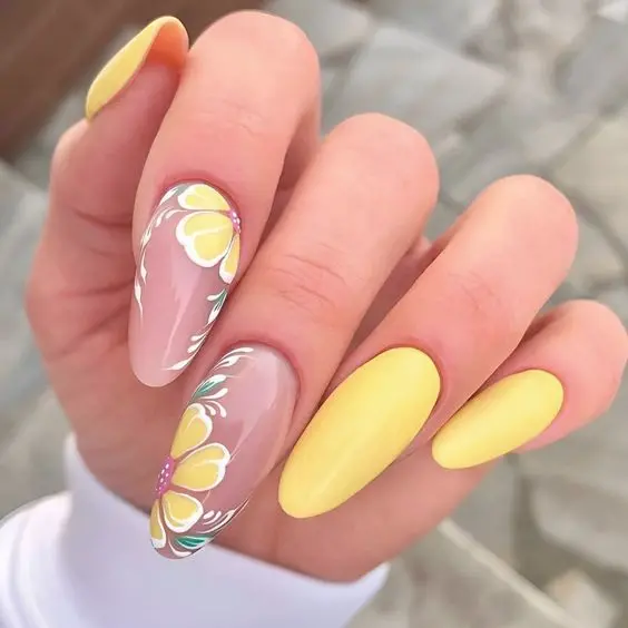 These nails feature a summer-perfect yellow with almond shapes and floral accents. The clear base on the accent nails highlights detailed yellow and white flowers, creating a fresh and vibrant look, perfect for embracing the sunny season.