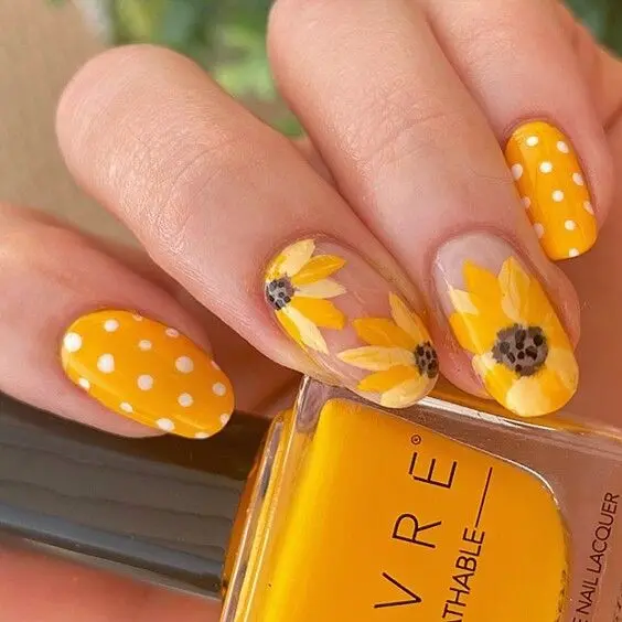 These nails feature an oval shape with bright yellow polish and sunflower designs on the accent nails. The combination of clear bases, detailed flowers, and polka dots creates a playful and vibrant summer look.