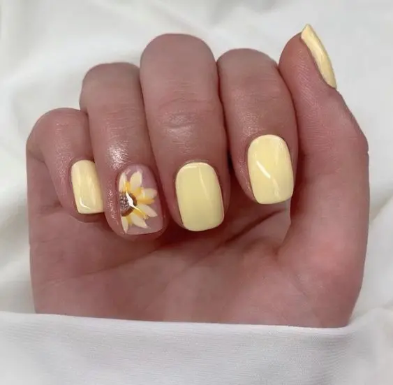 These short, square nails have a pastel yellow polish with an accent nail featuring a detailed sunflower. The design is simple yet striking, capturing the essence of summer with its bright, sunny color and floral touch.