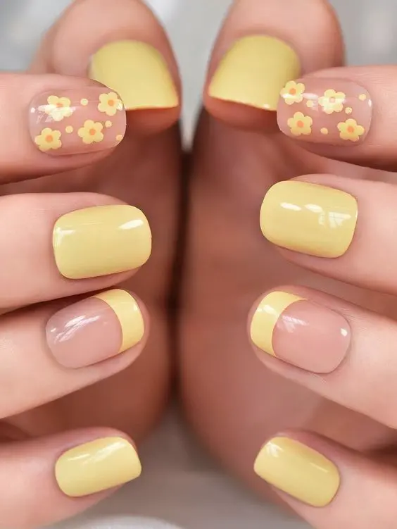 Squoval-shaped nails adorned with yellow French tips and tiny floral patterns evoke a cheerful summer vibe. The combination of solid yellow and transparent floral accents adds a playful and elegant touch, ideal for warm weather.