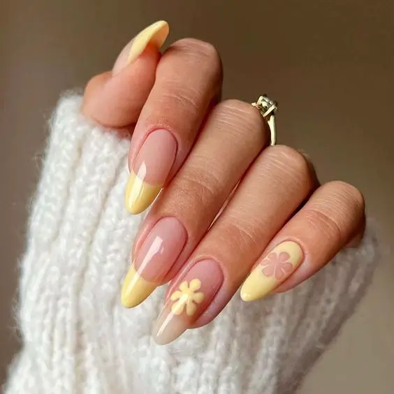 This set showcases a subtle yet elegant design with light yellow French tips and accent flowers. The almond-shaped nails with clear bases and pastel floral accents create a soft and feminine look, perfect for a delicate summer style.