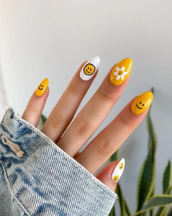 These nails feature a playful summer design with yellow smiley faces and white flowers. The almond-shaped nails combine vibrant yellow and white, bringing a fun and happy vibe, perfect for brightening up any summer outfit.