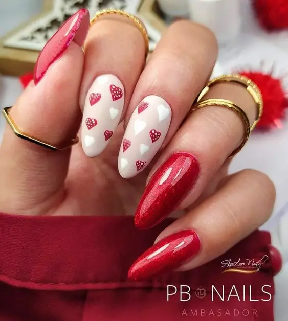 This playful design showcases red glitter nails and white accent nails adorned with red and white hearts. The almond-shaped nails create a fun and whimsical look, perfect for expressing love and joy.