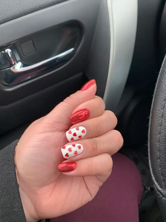 A chic red heart nail design features glossy red nails paired with white accents adorned with small red hearts. The squoval shape and high-shine finish offer a sophisticated look, symbolizing love and passion, perfect for romantic occasions.