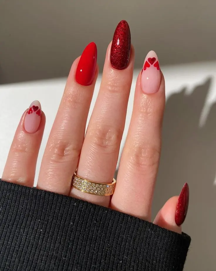 This red heart nail design showcases glossy red nails paired with a glitter accent nail and heart details on a nude base. The almond shape enhances the elegant and sophisticated look, ideal for adding a touch of glamor and romance to any outfit.