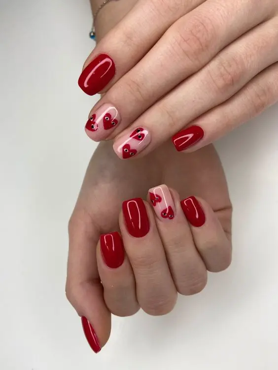 This stylish manicure features a deep red base with nude accent nails, each adorned with red hearts. The square shape and glossy finish highlight a modern and elegant design, perfect for adding a romantic touch to any outfit.