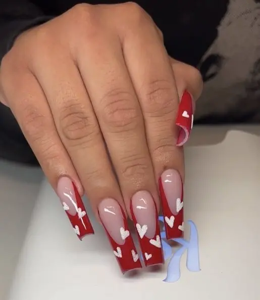 These stylish ballerina-shaped nails have bold red French tips and white heart accents. The nude base enhances the vibrant red and creates a chic and romantic design, perfect for special occasions.