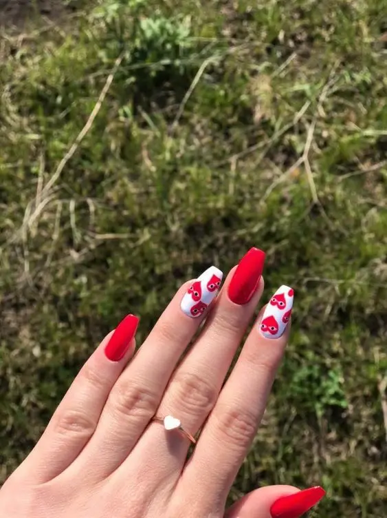 These adorable nails feature bright red polish and white accent nails with playful red heart faces. The ballerina shape and fun design make it perfect for a youthful and cheerful look.