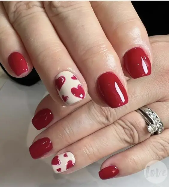 This red heart nail design features a combination of solid red and nude nails, adorned with small red hearts. The square shape and glossy finish provide a stylish, romantic look perfect for Valentine\'s Day or any love-themed occasion.