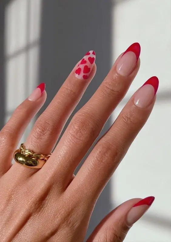 These chic red heart nails feature a refined French tip design with a touch of romance. The almond-shaped nails are adorned with red tips, and one nail stands out with red heart patterns, symbolizing love and passion.