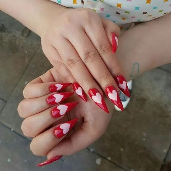 These long, pointed nails are painted in a vibrant red with nude accent nails decorated with small hearts. The bold and striking stiletto shape complements the romantic design, perfect for special occasions.