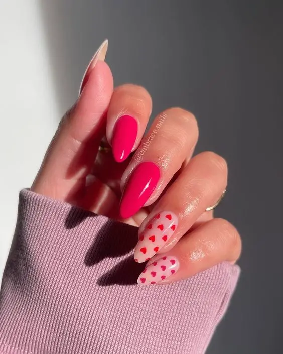 These vibrant almond-shaped nails feature a mix of solid pink polish and nude accent nails adorned with tiny red hearts. The playful design and bright colors make it perfect for adding a touch of fun and romance to any look.