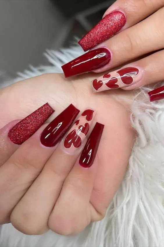 These glamorous ballerina-shaped nails feature a combination of red glitter, glossy red polish, and clear accent nails with red heart designs. The mix of textures and heart patterns creates a sophisticated and festive look.