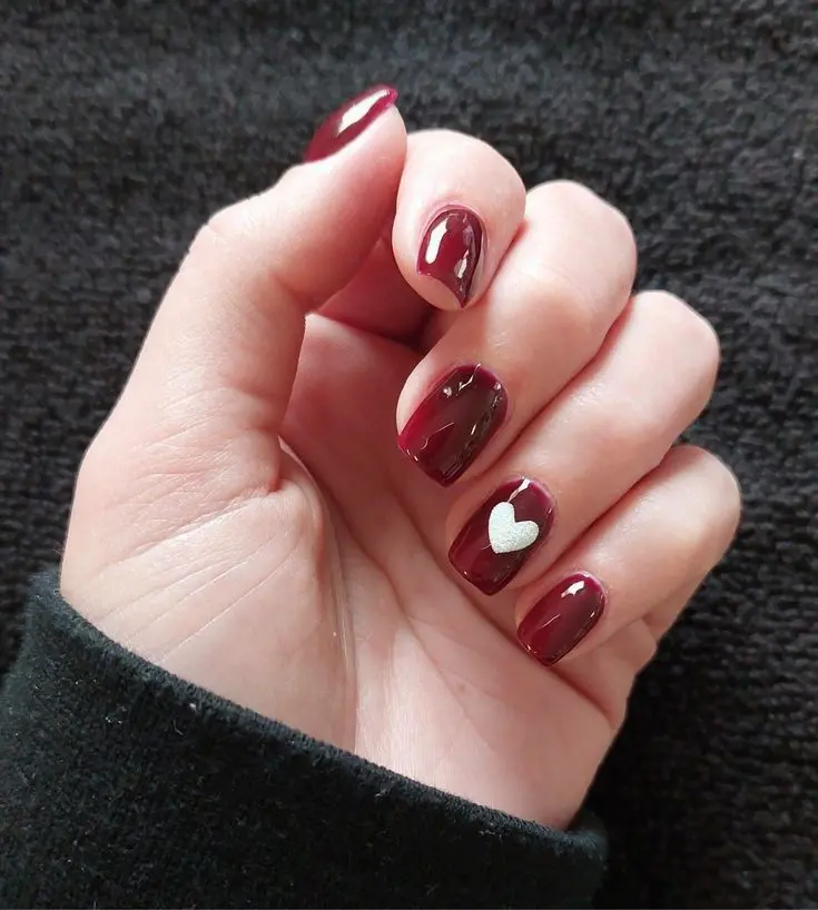 This nail design features dark red polish with a single silver heart accent. The deep red color exudes sophistication, while the heart adds a sweet and romantic touch, making it suitable for both formal and casual occasions.