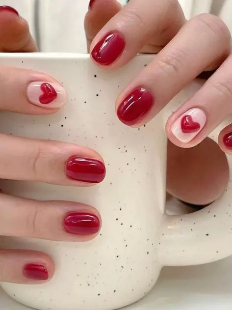 This elegant nail art combines deep red polish with nude accents, each highlighted by a bold red heart. The minimalist squoval shape and glossy finish make these nails ideal for expressing subtle romance and charm.