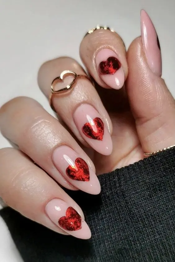 Elegant and bold, these red heart designs on a light pink base accentuate the sharp, pointed nails with a glossy finish. The heart motif, placed at the center of the nail, highlights the stylish beauty.