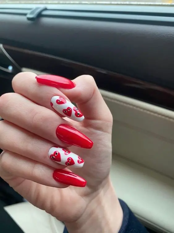 These playful nails feature bright red polish and white accent nails with cute red heart faces. The ballerina shape and fun design add a whimsical touch, perfect for expressing joy and affection.