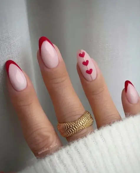 These elegant almond-shaped nails feature red French tips and a single nail with a trio of tiny red hearts. The design combines simplicity with a touch of romance, perfect for a subtle yet charming look.