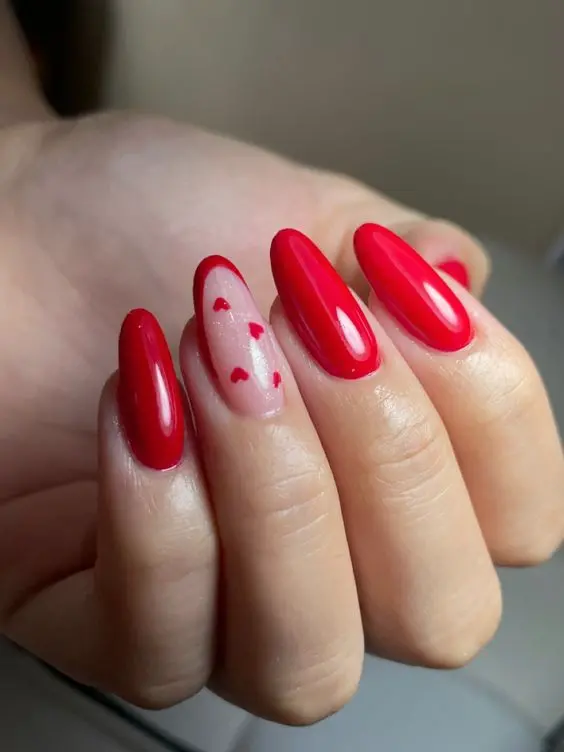 This glossy red nail design features almond-shaped nails with a single nude accent nail decorated with tiny red hearts. The bold red color and subtle heart accents create a stylish and romantic look.