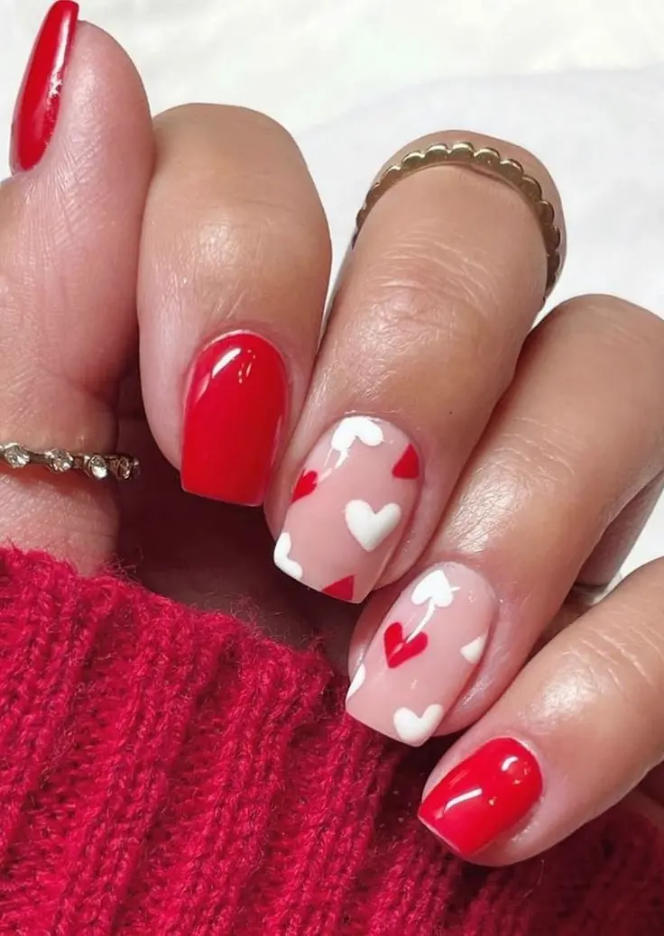 This nail design showcases a mix of solid red glossy nails and nails with nude bases decorated with large red heart accents. The square shape adds a touch of simplicity and elegance, making it suitable for both everyday wear and special events.