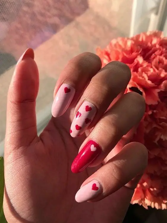 These romantic almond-shaped nails showcase a mix of soft pink and red, with heart patterns on two accent nails. The combination of colors and heart designs symbolizes love and affection, making it perfect for any romantic occasion.