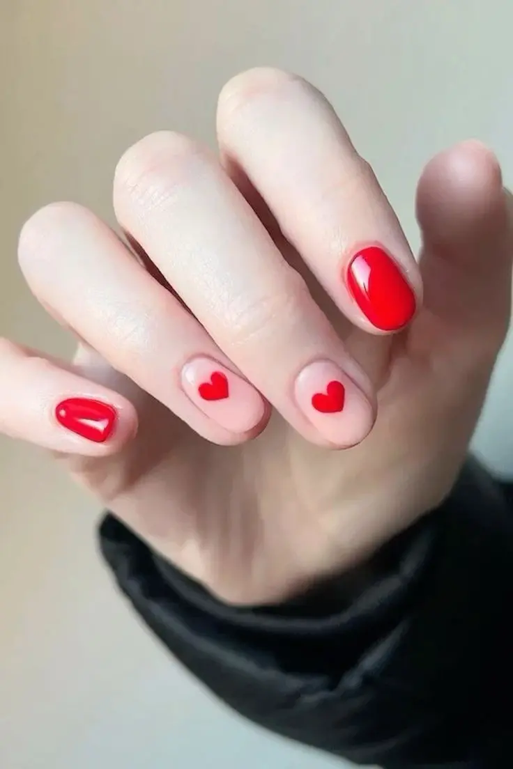 Short, glossy red nails are elevated by playful heart accents on a nude base. The oval shape and vibrant red polish create a fun yet sophisticated look, symbolizing love and joy, ideal for everyday wear.