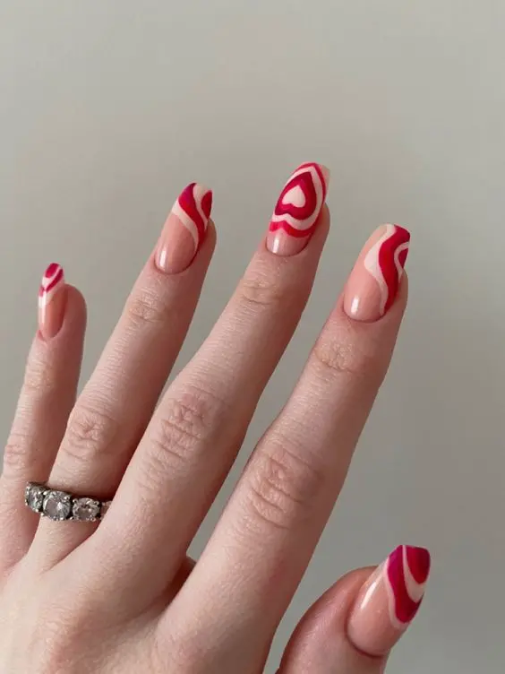 These ballerina-shaped nails showcase a unique abstract design with red and pink swirls forming heart patterns. The modern and artistic style adds a creative touch to the classic red heart theme.