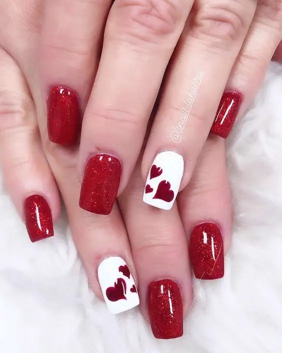 This nail design features a striking combination of sparkling red glitter and crisp white. The white accent nails are adorned with elegant red heart motifs, adding a touch of romance and charm. The square shape provides a modern look, perfect for festive occasions or a glamorous night out.