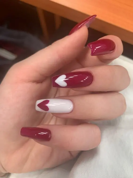 These stylish ballerina-shaped nails feature a combination of glossy red polish and white accent nails with red and white hearts. The bold colors and classic heart designs create a timeless and romantic look.