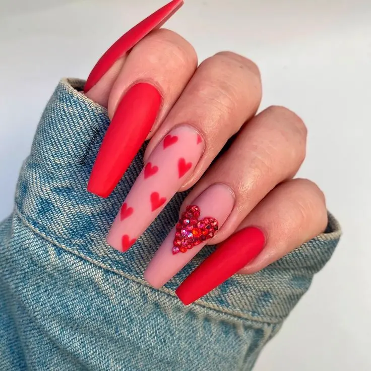 These vibrant ballerina-shaped nails combine matte red polish with accent nails featuring red hearts and glitter. The mix of textures and bold colors creates a striking and festive look, perfect for special occasions.