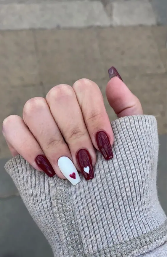 These elegant ballerina-shaped nails showcase a rich, deep red polish with a single white accent nail adorned with tiny red and white hearts. The sophisticated color scheme and minimalist heart details convey understated elegance and romance.